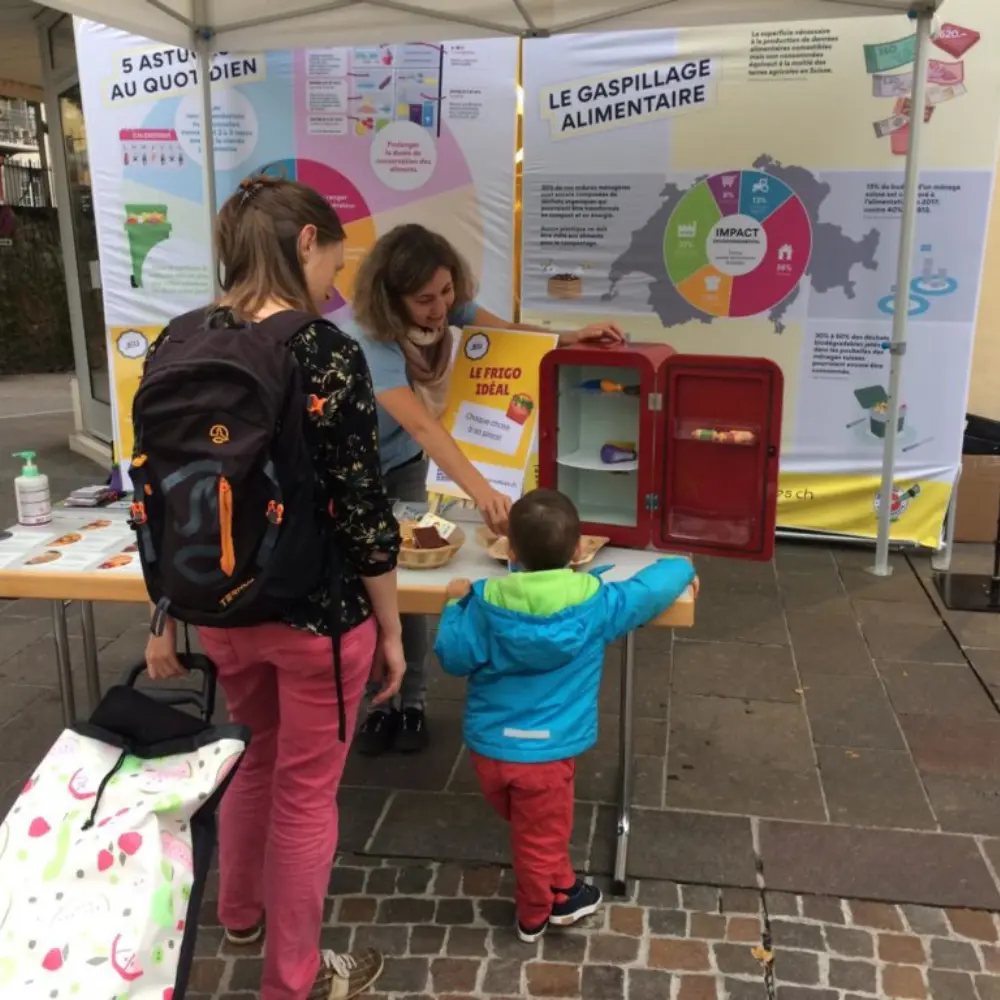 Une animatrice présente à une famille un stand de sensibilisation au gaspillage alimentaire.
