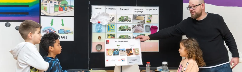 Un animateur COSEDEC présente le cycle du recyclage à des enfants dans le cadre de l’animation scolaire De l’or dans nos poubelles.